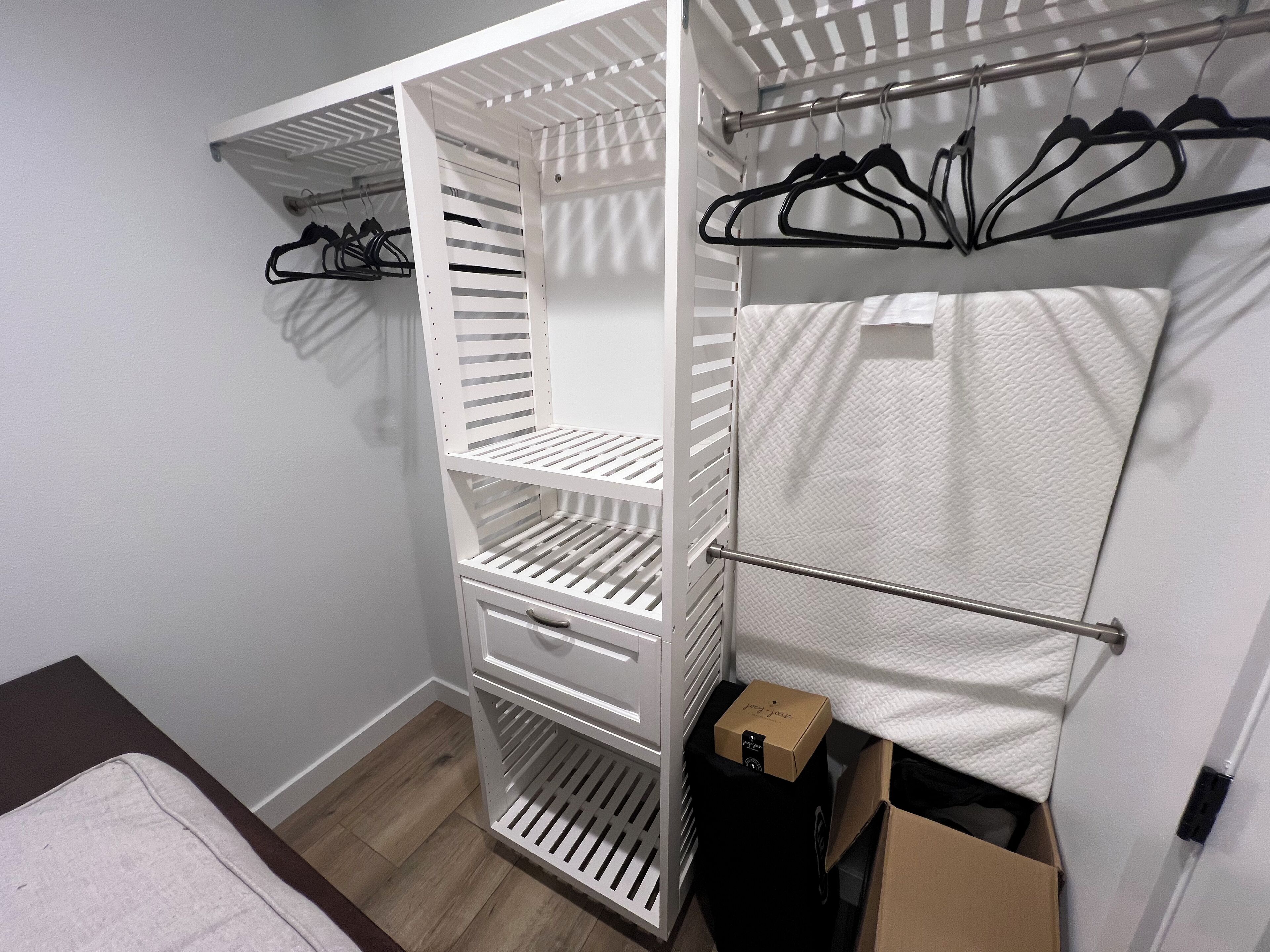 A white closet with multiple shelves and hanging space, a wooden floor, and a white wall.