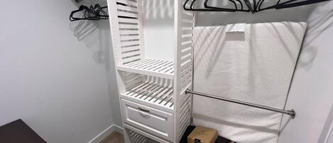 A white closet with multiple shelves and hanging space, a wooden floor, and a white wall.