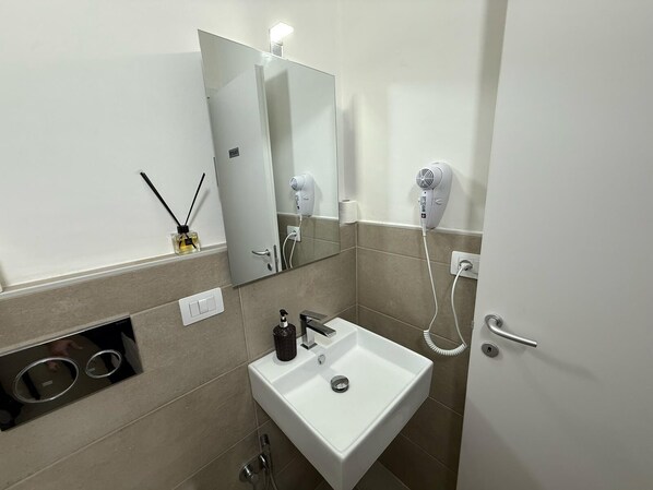 A modern bathroom with a white sink, a mirror, a hairdryer, and a bottle of hand soap. - Best Bnb Barbadori (Florence)
