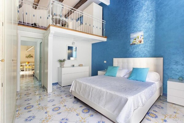 A bedroom with a bed, nightstands, a dresser, a balcony, and a blue accent wall.