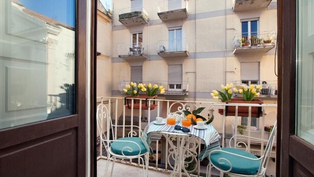 A balcony with a table set for two, featuring a striped tablecloth, two chairs with teal cushions, and a vase of yellow flowers. - Marescala vacation - Tarantino House, cozy apartment in the historic center (Sorrento)