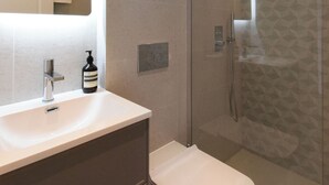 Une salle de bain moderne avec un lavabo blanc, un miroir, des toilettes et une douche séparée par une paroi en verre.