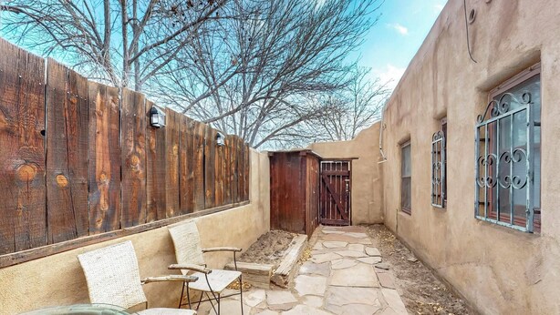 A courtyard with stone flooring, a wooden fence, and a rustic building with barred windows. - Inviting Remodeled Guest House in Central Nob Hill (Albuquerque)