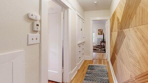 A hallway with white walls, a wooden floor, and a patterned rug. There are two white doors and a white thermostat on the wall. - Inviting Remodeled Guest House in Central Nob Hill (Albuquerque)