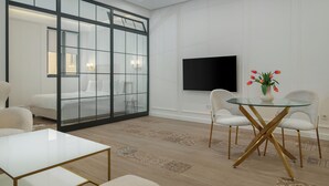 Ein modernes Zimmer mit Glastrennwand, einem Flachbildfernseher, einem runden Glastisch mit goldenen Beinen und einer Vase mit Tulpen.
