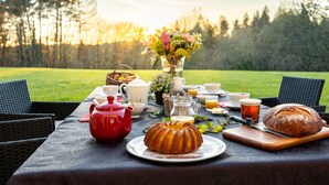 A picnic setup with a table set for breakfast, including a red teapot, a bundt cake, a loaf of bread, and various breakfast items. - Bed and breakfast Le Rucher des Combes - Chambre Vézère (Fleurac)