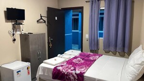Une chambre d’hôtel équipée d’un lit, d’une armoire, d’une télévision et d’un petit réfrigérateur.