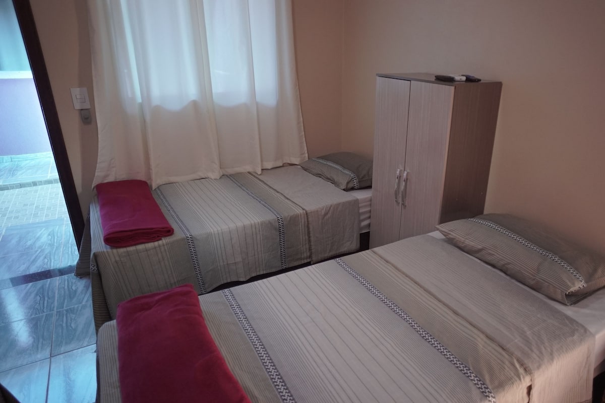 A hotel room with two single beds, a wardrobe, and a window with curtains.
