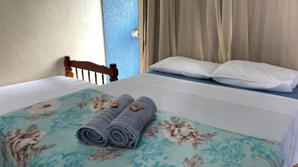 A bed with a floral bedspread, two rolled towels, and a wooden headboard.