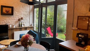 A cozy room with a dining table, chairs, a coffee machine, and a large window with a view of the garden. - La Grange du Manoir (eco-cottage for 2–4 people) (Le Vieux-Marché)