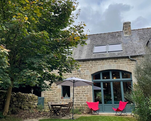 A stone house with a patio, a table, two chairs, and an umbrella.