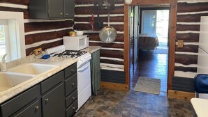 Cocina de cabaña de troncos con piso de piedra, estufa a gas, pileta y microondas.