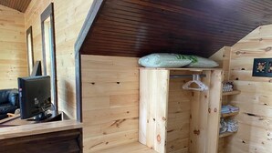 Interior de una cabaña de madera con escritorio, ordenador y banca.