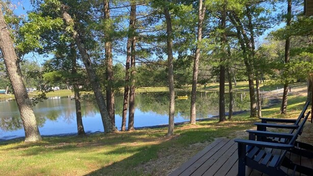 Una terraza de madera con un banco da a un lago tranquilo, rodeado de árboles.