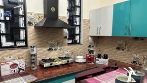 Una cocina con estufa a gas, extractor de humos y diverso menaje de cocina. Hay armarios, una encimera y un salpicadero.