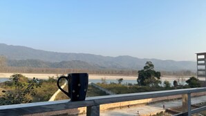 Una taza sobre la barandilla de un balcón con vistas a un río y montañas.