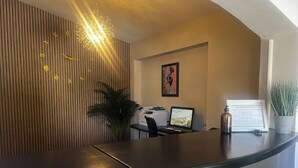 Un comptoir d’accueil au design moderne, un ordinateur portable, un panneau encadré indiquant les heures d’ouverture de l’accueil et une plante en pot.