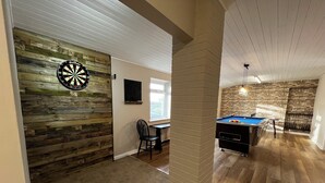 Une pièce avec un jeu de fléchettes, une table de billard et un mur en bois.