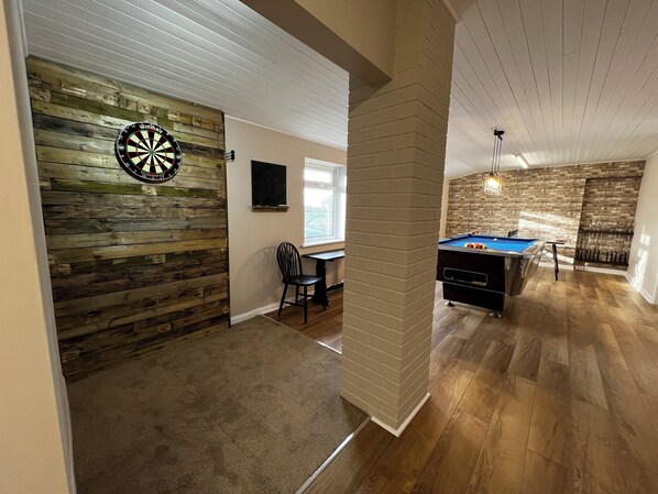 A room with a dartboard, a pool table, and a wooden wall.
