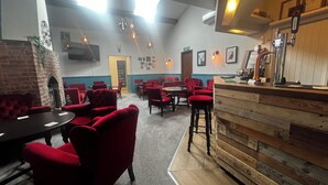 Un restaurant chaleureux avec des chaises à l’assise rembourrée de tissu rouge, un comptoir de bar en bois et des luminaires suspendus.