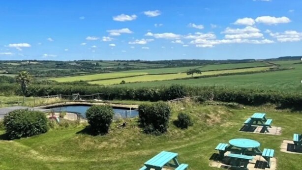 Un paysage rural avec un étang, des tables de pique-nique et un ciel bleu dégagé.