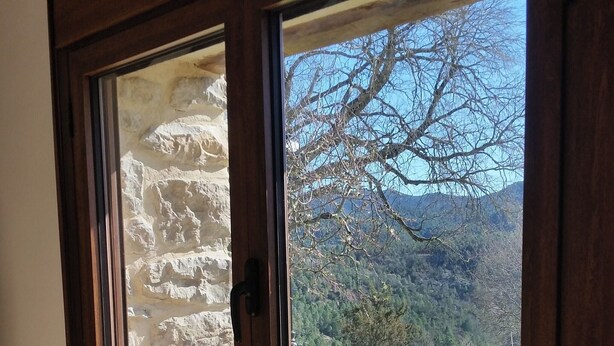 A room with a large window revealing a stone wall, a view of a green landscape, and a chair in the foreground. - Casa Alegria de Lamata. Newly built, ground floor, accessible. (Lamata)