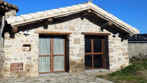A stone building with a tiled roof, two wooden doors with curtains, and a small window. - Casa Alegria de Lamata. Newly built, ground floor, accessible. (Lamata)