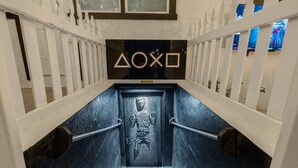 Un escalier au motif noir et blanc, menant à une porte sur laquelle figure un symbole géométrique.