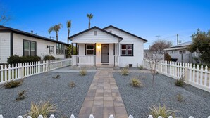 Une maison de plain-pied avec un porche à l’avant, une allée en gravier et une clôture blanche en bois.