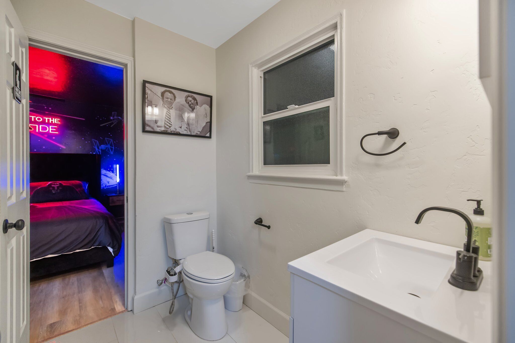 A compact bathroom with a white sink, a window, and a toilet.