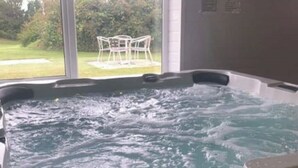 A hot tub with a view of a patio area and greenery outside.