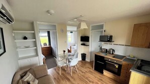 A compact living space with a kitchenette, a dining area with a glass table, and a sofa.