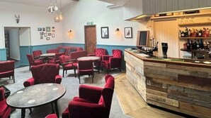 A bar area with red upholstered chairs and tables, wooden bar counter, and wall-mounted lights.