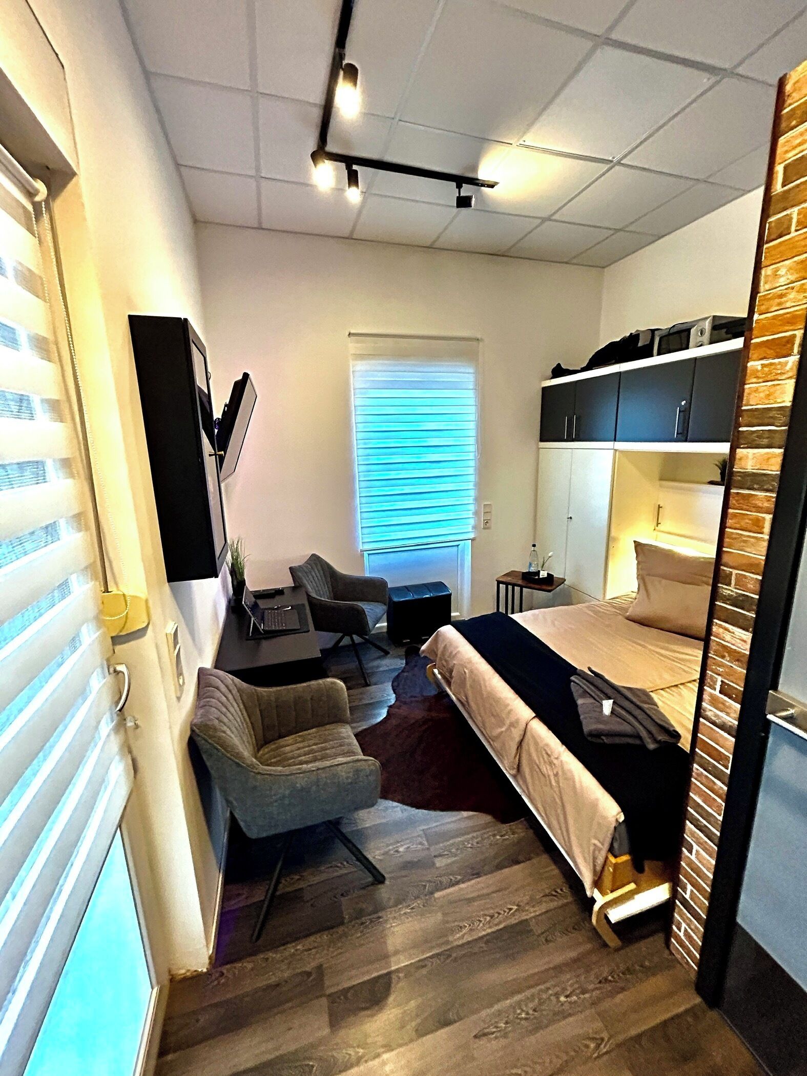 Une chambre d’hôtel de taille réduite, comprenant un lit, un bureau, une chaise et une armoire.
