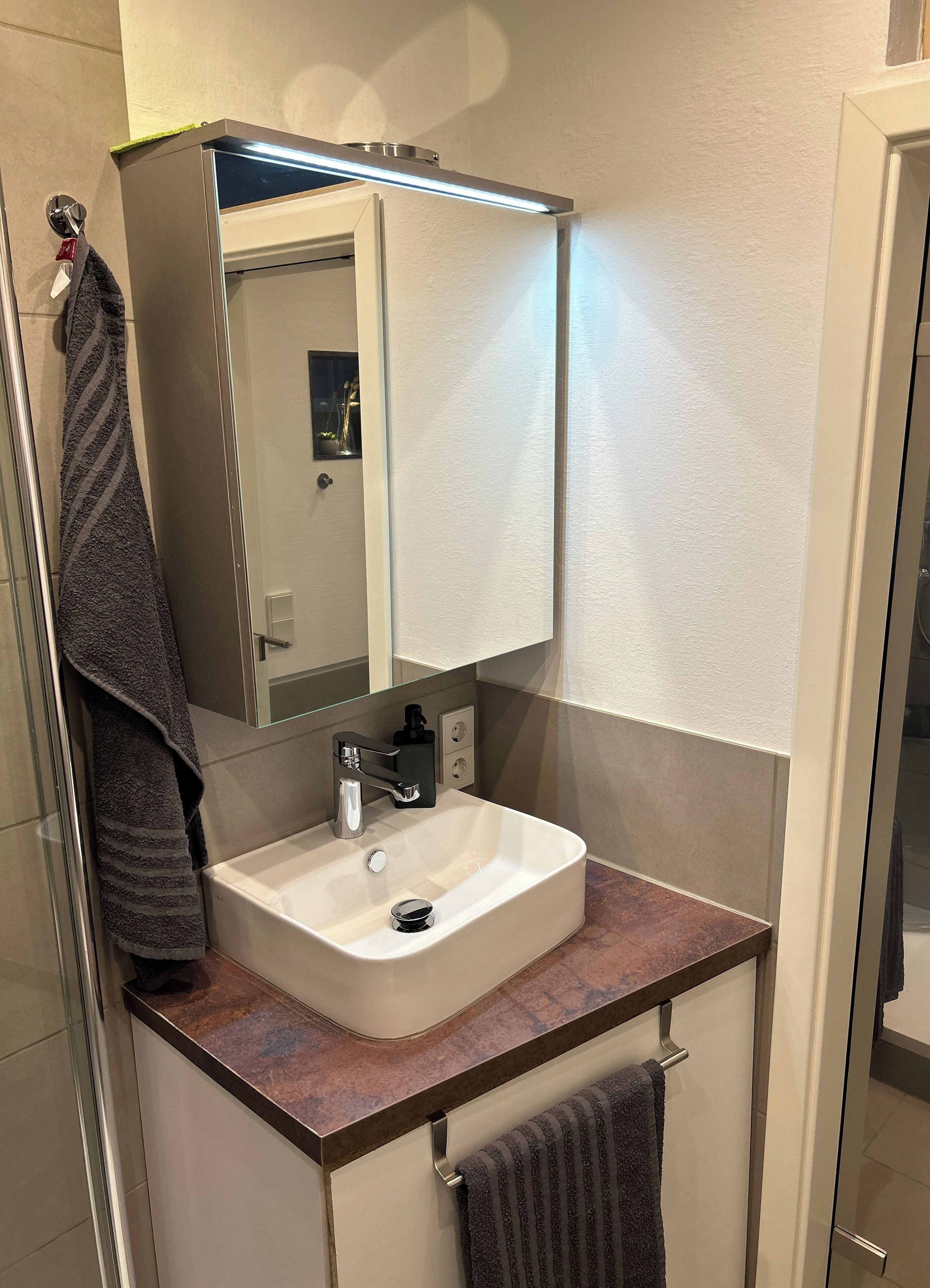 A modern bathroom with a white sink, a mirror above it, and a towel hanging on a rack.