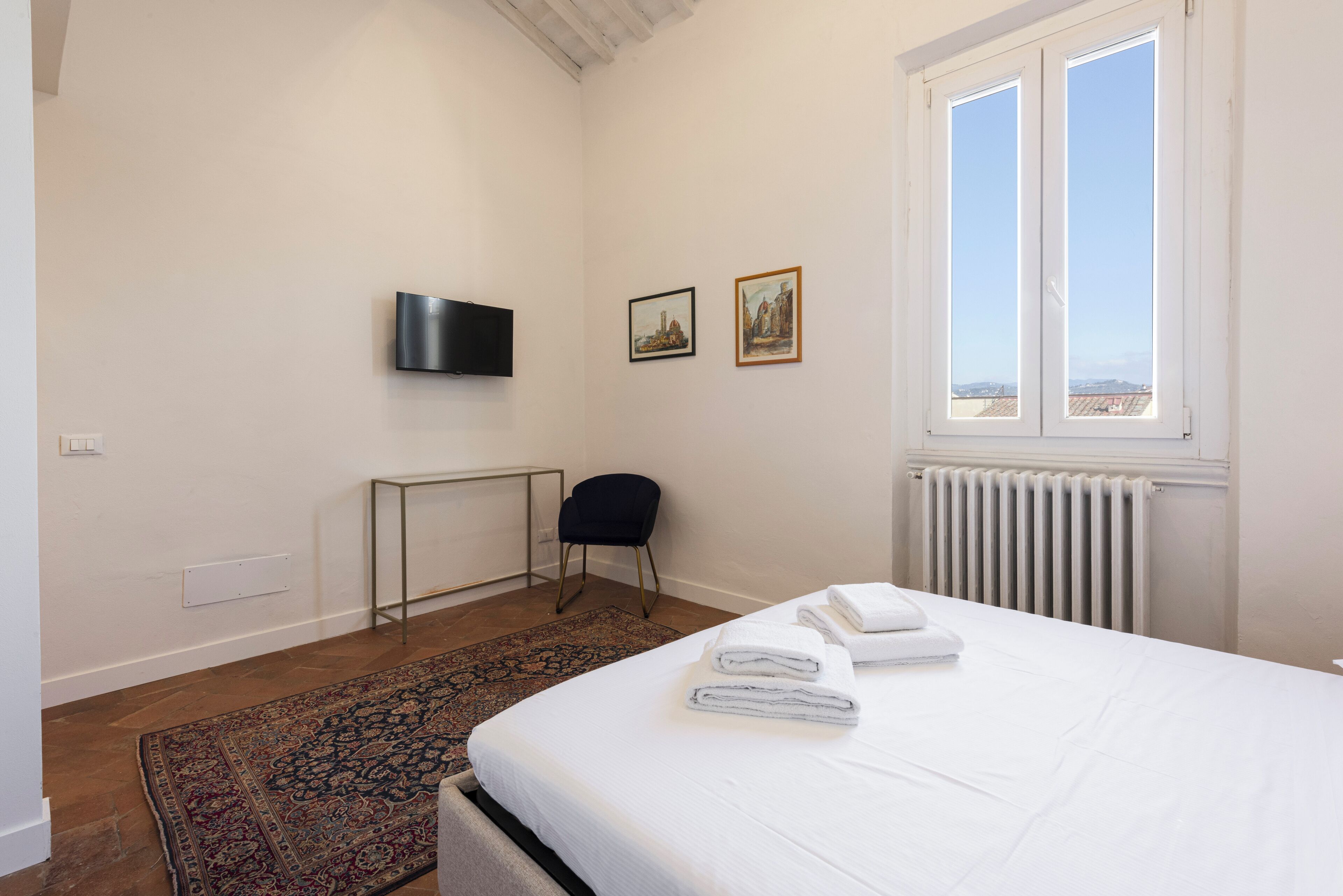Quarto de hotel com cama, escrivaninha, cadeira, televisão e janela com vista.