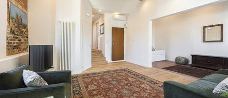 A spacious living area with a large rug, two green sofas, a television, and a staircase leading to another room.