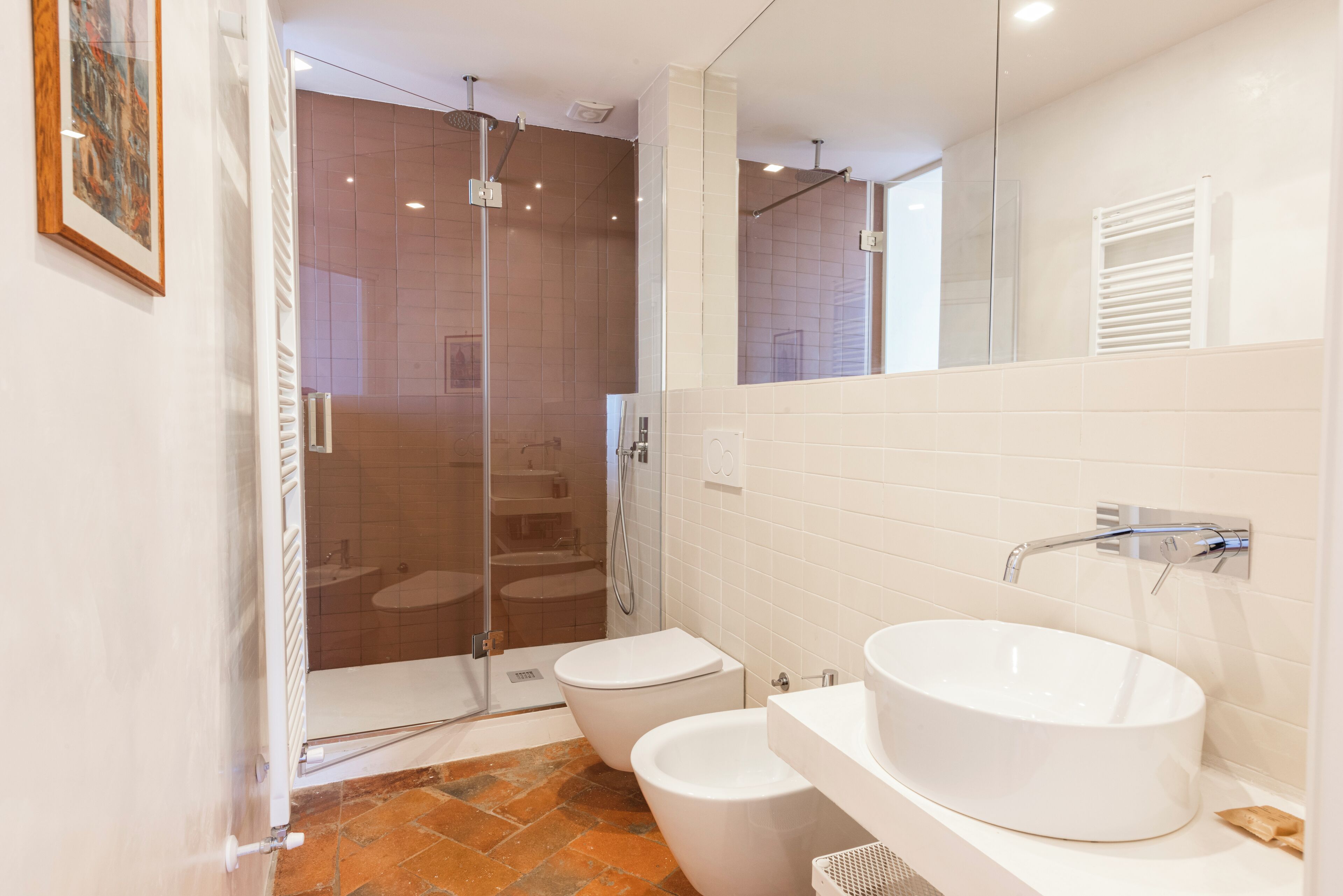 A modern bathroom with a glass-enclosed shower, two toilets, and a large oval sink.