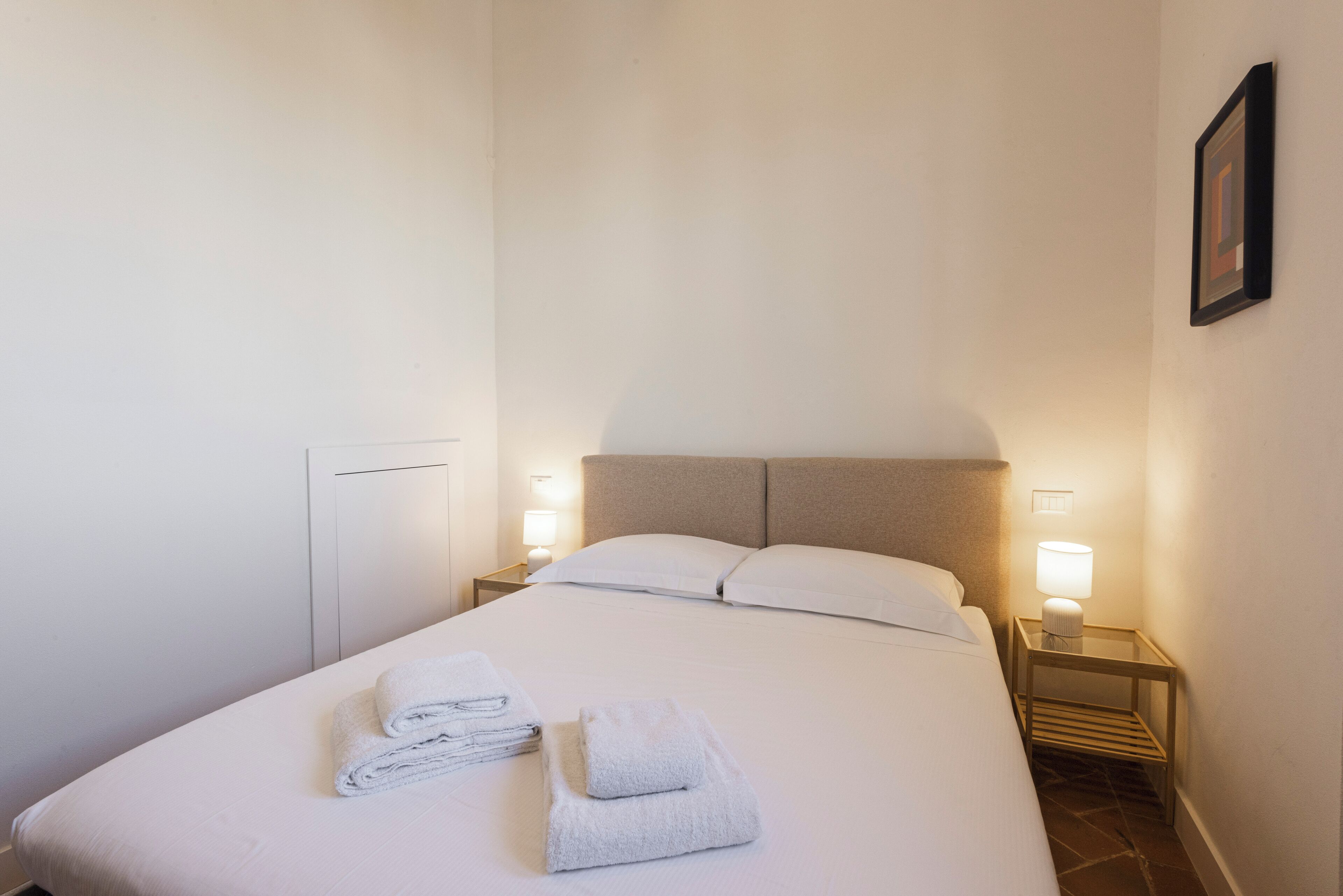 Un lit bien fait, avec des serviettes pliées, une tête de lit et des lampes de chevet.