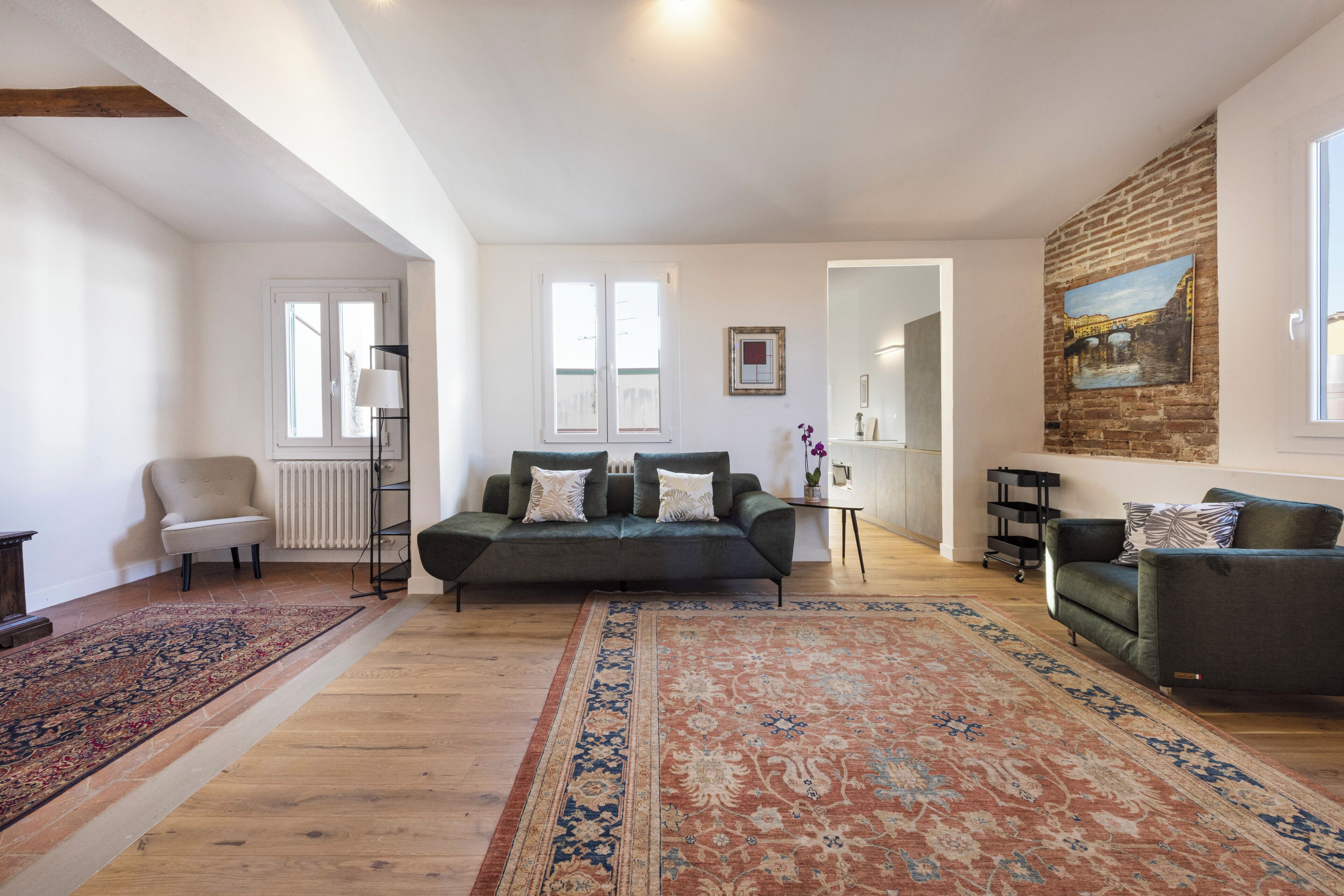 Een ruime woonkamer met een groot tapijt, twee banken, een salontafel en een schilderij aan de wand.