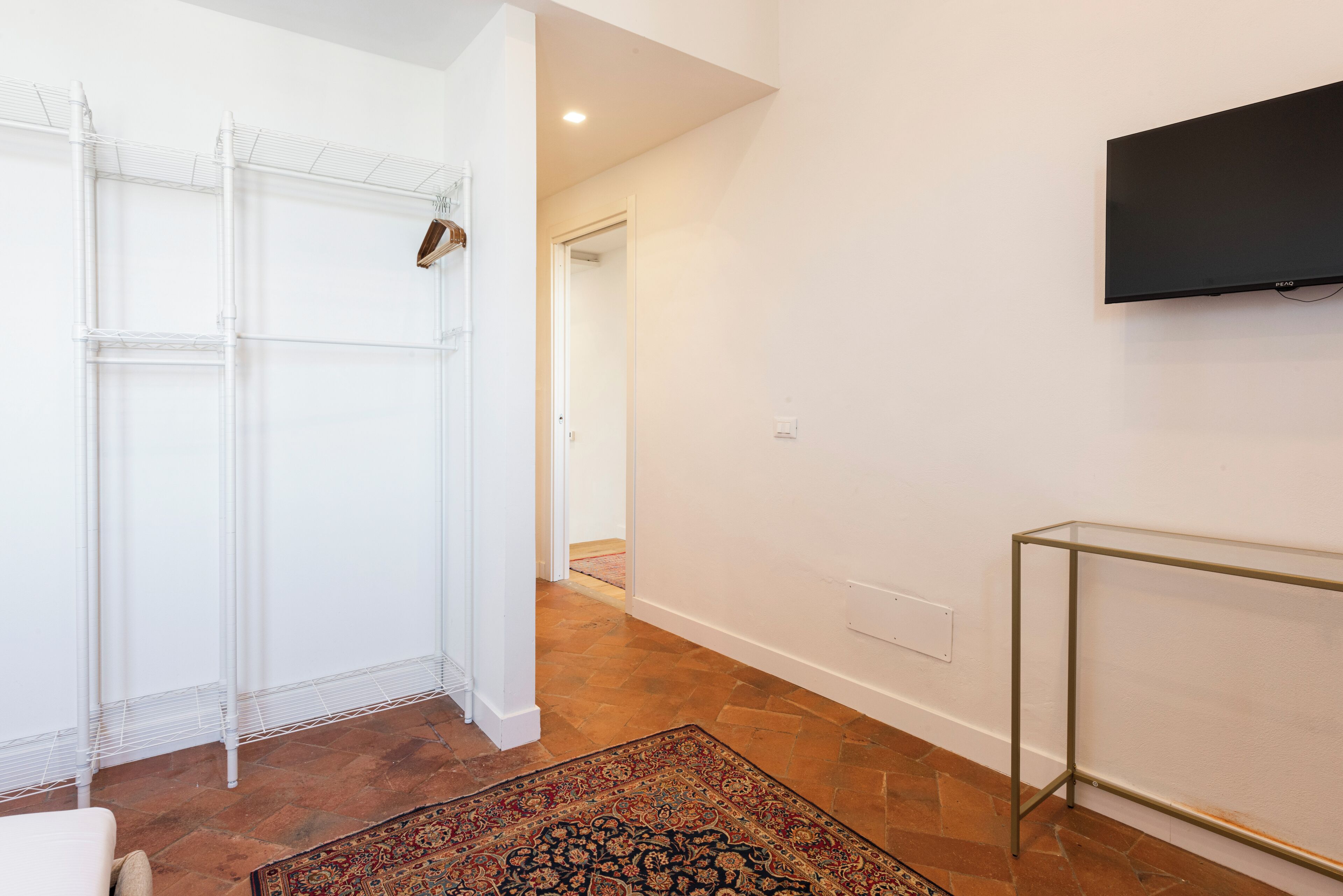 A hallway with a white closet, a patterned rug, and a TV mounted on the wall.