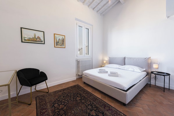 A bedroom with a bed, a chair, a window, and two framed pictures on the wall. - Santa Maria Novella penthouse by MMega (Florence)