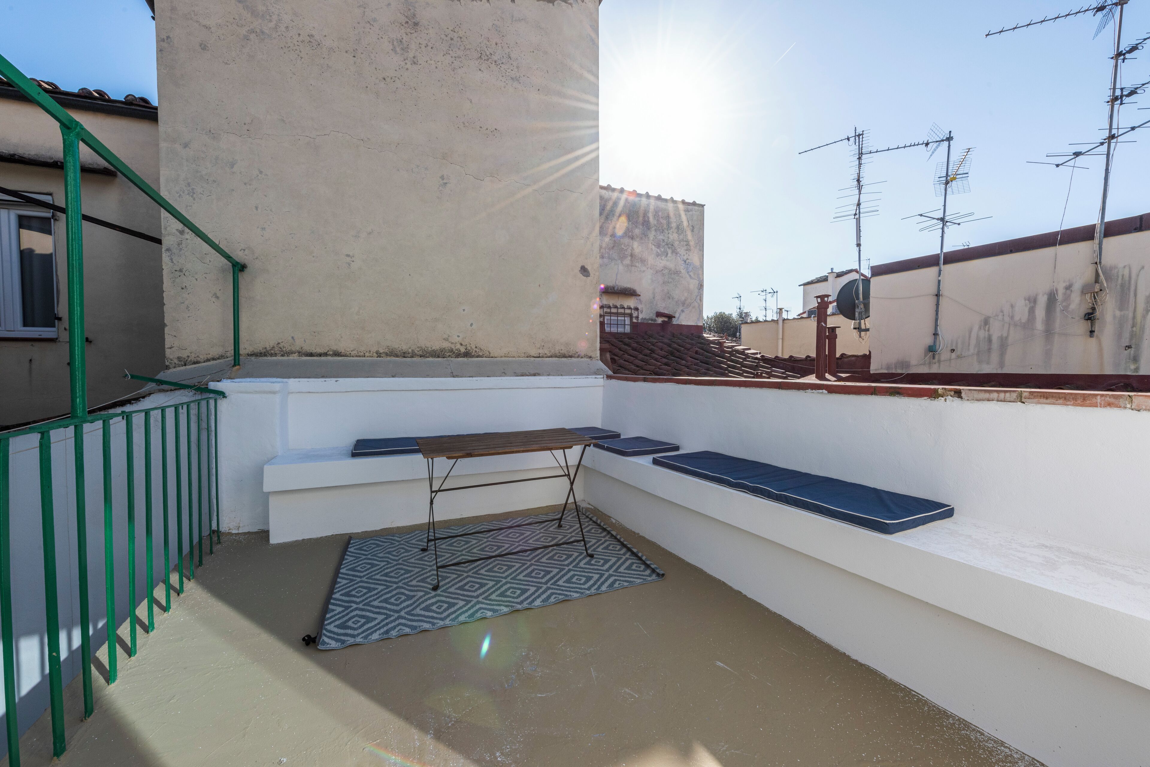 Eine Dachterrasse mit Tisch, Bänken und einer gemusterten Matte.