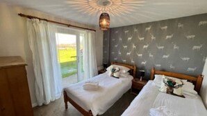 Une chambre avec deux lits, une grande fenêtre avec des rideaux, un lustre et un mur orné d’un motif représentant des animaux blancs.