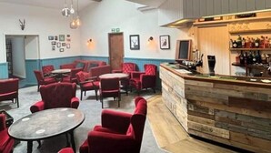 Un área de bar acogedora con sillas y mesas tapizadas en rojo, una barra de madera y cuadros enmarcados en las paredes.