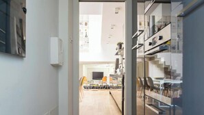Moderni keittiö, jossa on keskeinen saareke, ruokailutila tuoleineen sekä portaikko, joka johtaa ylemmälle tasolle.