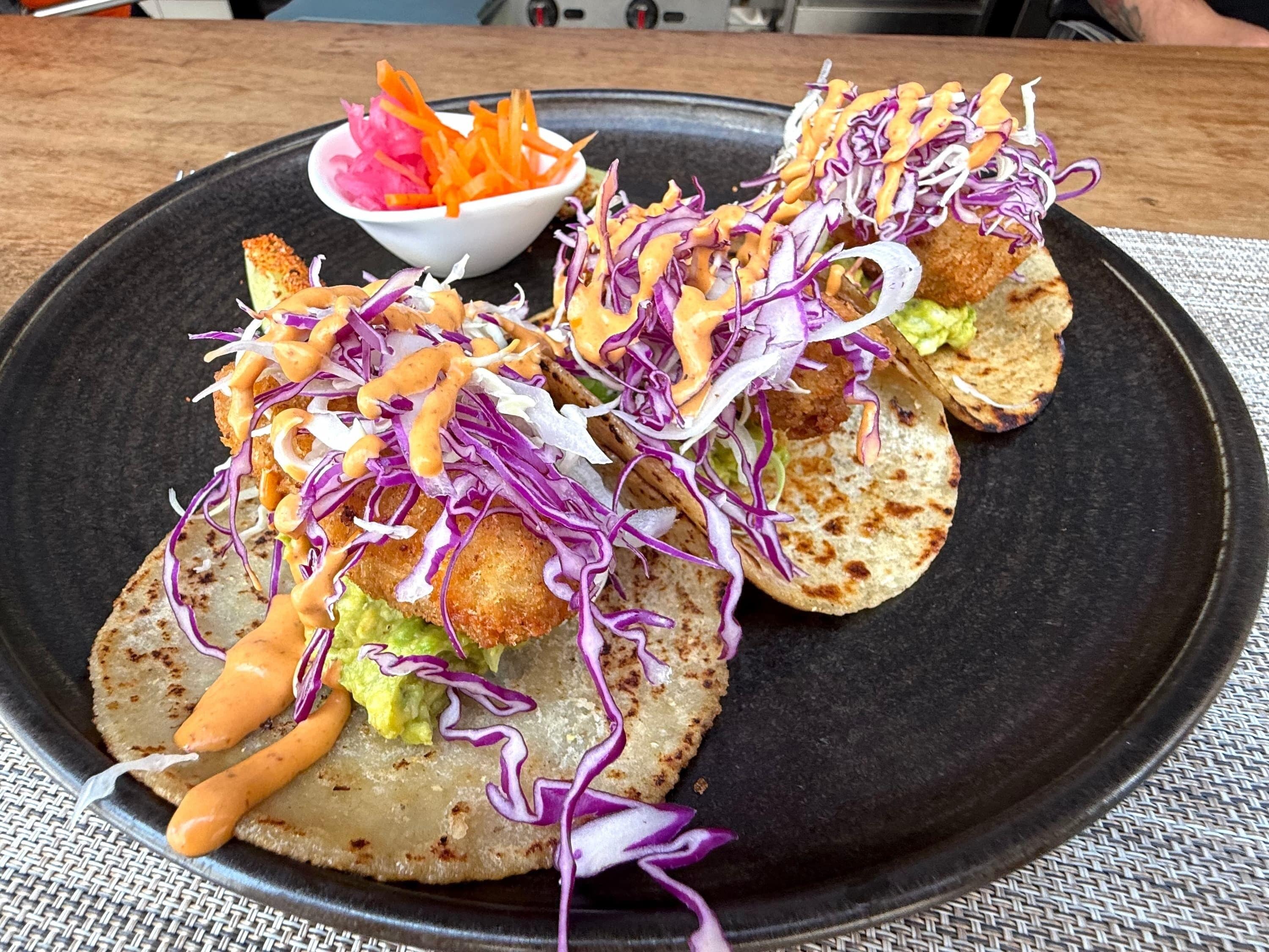 A plate of tacos with avocado and purple cabbage on a black plate.