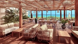 An outdoor seating area with wicker furniture, large windows, and a view of the ocean. - Windward Mayreau Resort (Mayreau Island)