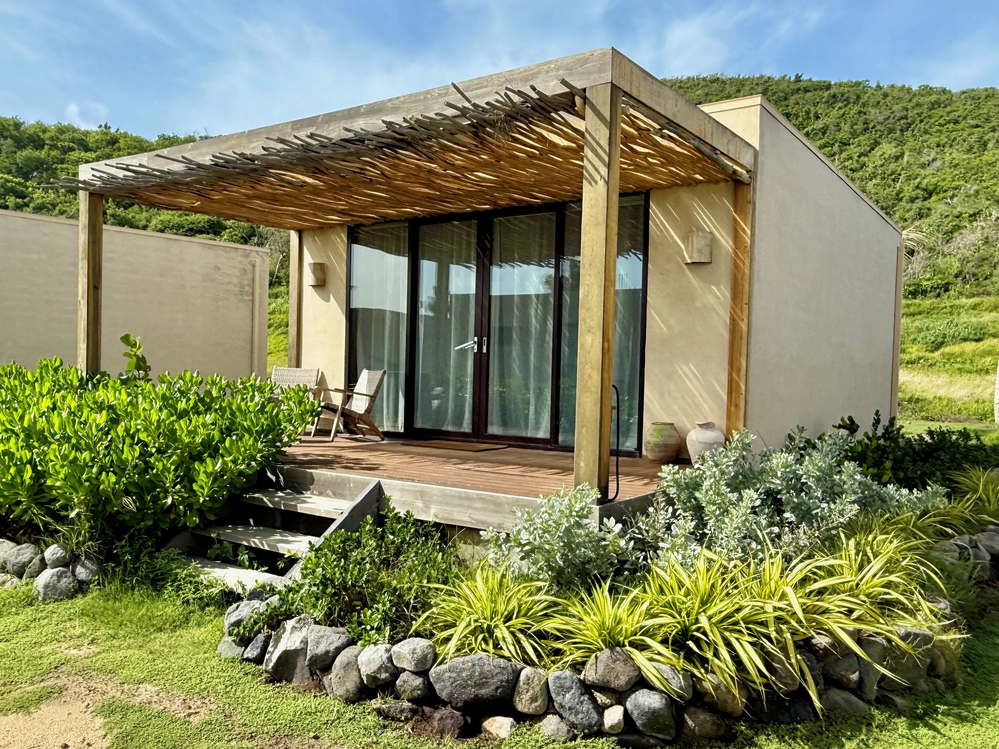 Une maison moderne dotée d’une terrasse en bois, d’un patio couvert et d’une porte vitrée donnant sur une pièce.