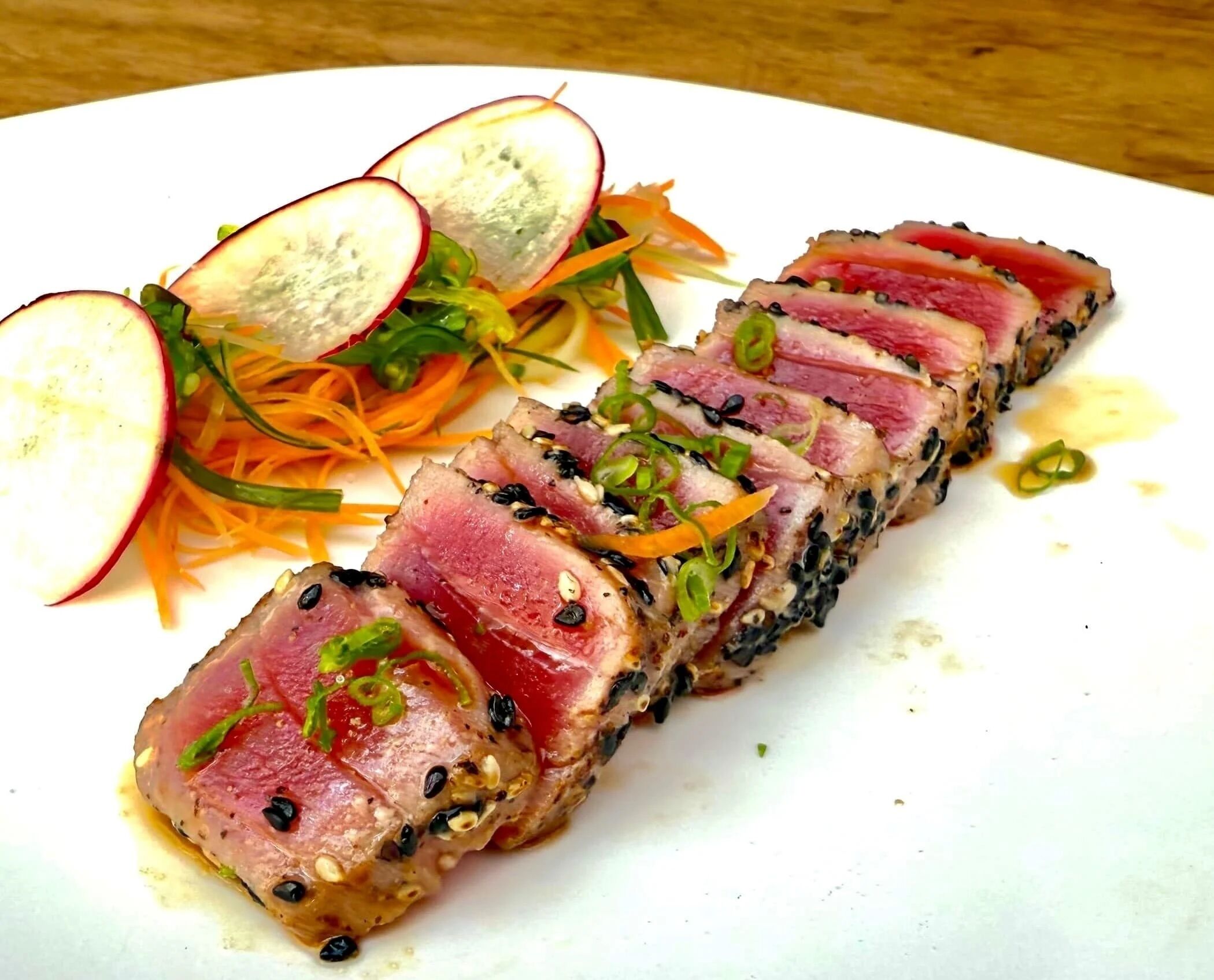 A plate of sliced tuna with sesame seeds, green onions, and radish slices.